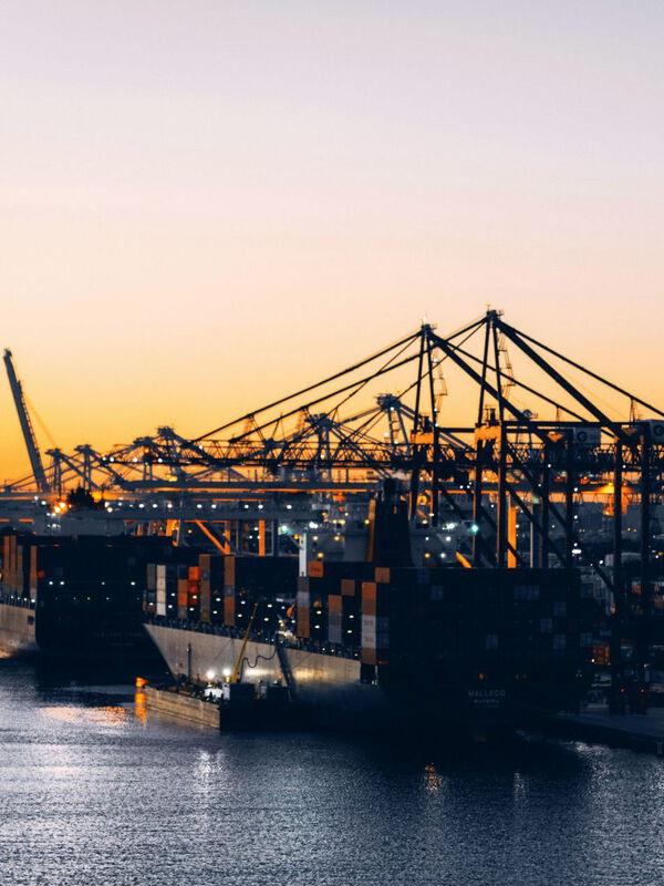 Blick in einen Containerhafen mit zwei Schiffen und Kränen im Sonnenuntergang